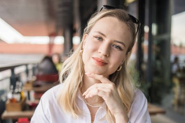 Kafe terasında çenesini dinlendiren genç bir kadının portresi. Sakin şehir hayatı, düşünceli ruh hali, kafeterya kültürü ve sakin şehir anı.