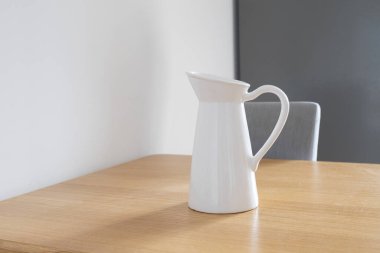 Mutfaktaki tahta masada beyaz sürahi. Ev sadeliği, durgunluk ve günlük hayat estetiği. Boşluğu kopyala.