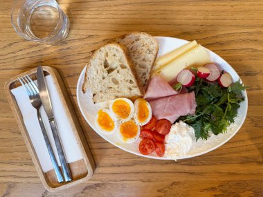 Yumurtalı, peynirli, jambonlu ve ahşap masada taze sebzeli kahvaltı tabağı. Dengeli beslenme, kahve servisi, temiz kompozisyon, sağlıklı yaşam tarzı..