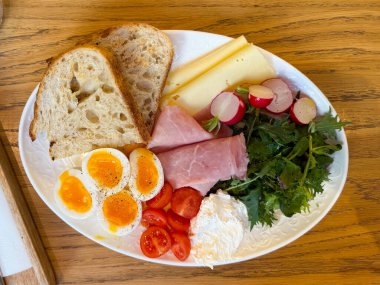 Yumurtalı, peynirli, jambonlu ve ahşap masada taze sebzeli kahvaltı tabağı. Dengeli beslenme, kahve servisi, temiz kompozisyon, sağlıklı yaşam tarzı..
