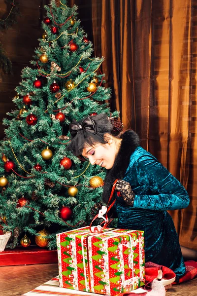 Feiertage, Feiern und Menschen-Konzept - lächelnde Frau im Kleid öffnet Geschenkbox über Christbaumhintergrund — Stockfoto