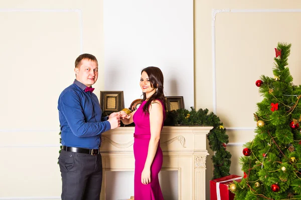 Queres casar comigo? Bonito jovem fazendo uma proposta enquanto dá um anel de noivado para sua namorada com decoração de Natal no fundo — Fotografia de Stock