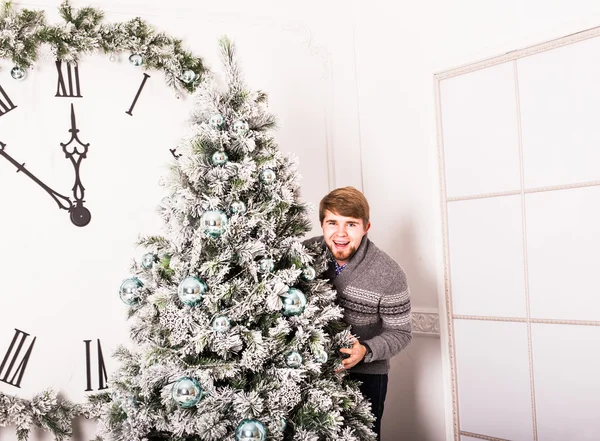 Jonge man die achter een kerstboom — Stockfoto