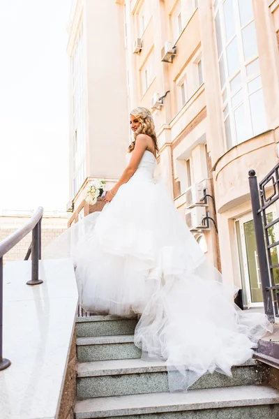 Beautiful bride in magnificent dress stands alone on stairs — Stock Photo, Image