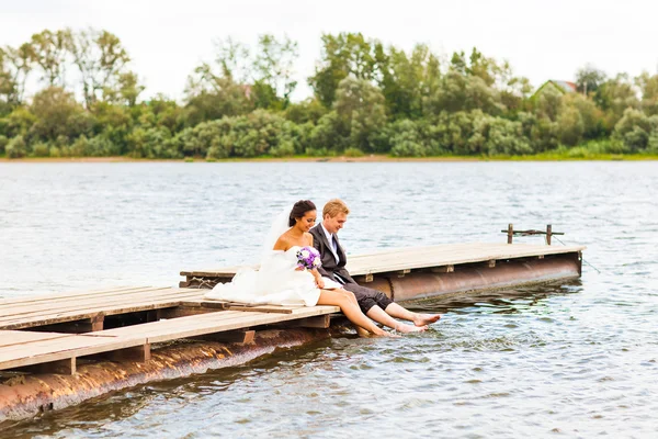Mooie bruid met de bruidegom door een meer. Kussen en omhelzen elkaar — Stockfoto