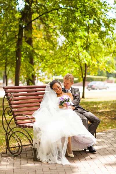 Noiva casamento elegante casal em vestido branco e elegante noivo sentado em um banco — Fotografia de Stock