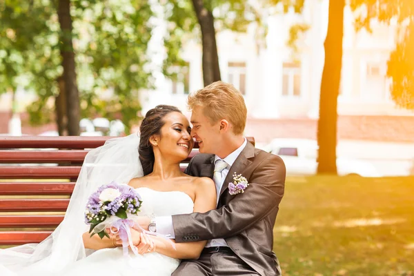 Sposa elegante coppia di nozze in abito bianco ed elegante sposo seduto su una panchina — Foto Stock