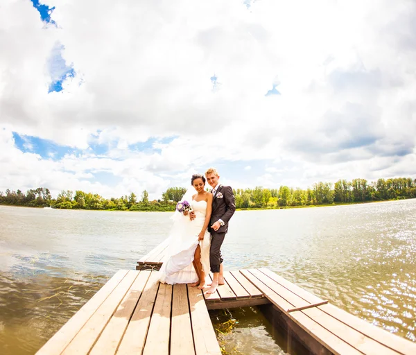 Mooie bruid met de bruidegom door een meer. Kussen en omhelzen elkaar — Stockfoto