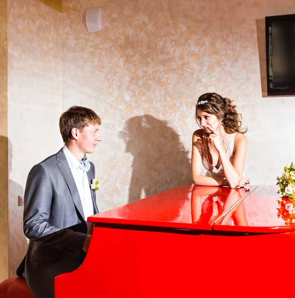 Charming wedding couple playing on a red piano in the room — Stock Photo, Image