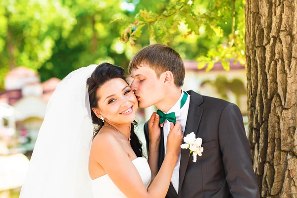 Glücklich lächelnde Brautpaare, die Spaß haben und sich am Hochzeitstag im Freien küssen. — Stockfoto