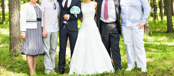 Casal recém-casado com convidados no parque ensolarado verde — Fotografia de Stock