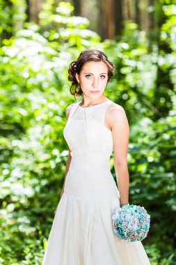 Gelinlikli genç gelin elinde buket tutuyor.