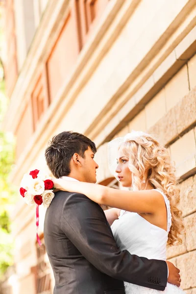 Svatební pár objímání, nevěsta drží kytici květin v ruce, ženich ji objímají — Stock fotografie