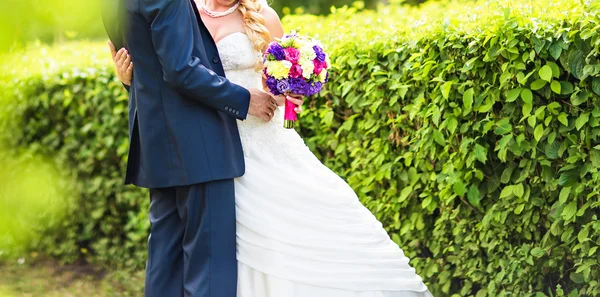 Para ślub przytulanie, panny młodej z bukietem kwiatów w ręku — Zdjęcie stockowe