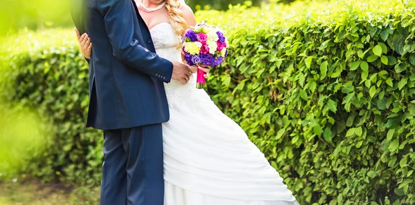 Casamento casal abraçando, a noiva segurando um buquê de flores em sua mão — Fotografia de Stock