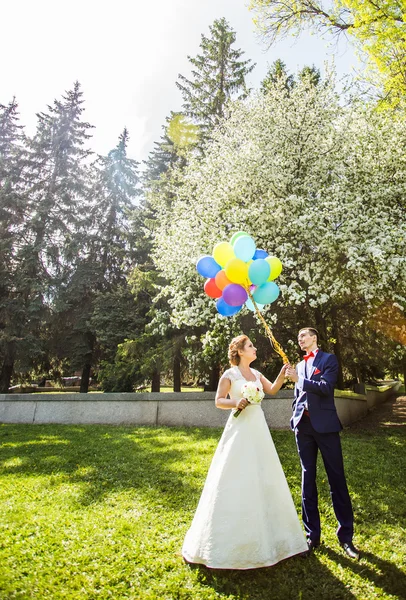 Happy bride and groom walking together in a spring park with balloons — Stock Photo, Image