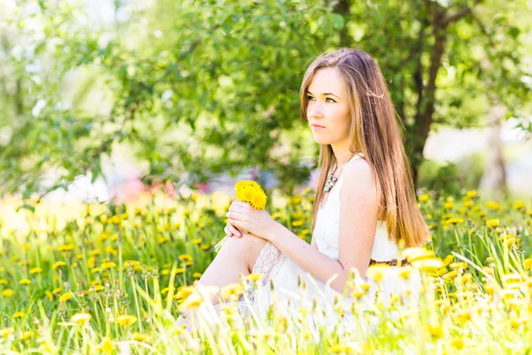 Portrait of beautiful girl with bouquet of yellow dandelions outdoor in summer, focus on eyes — Stock Photo, Image