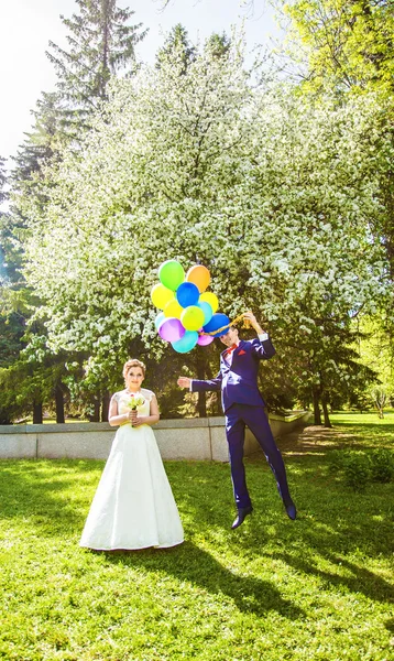 O noivo voa nos balões, mas a noiva segura a mão. Casamento engraçado. Groom salta e voa em balões. Jovem marido voando de sua esposa. Conceito de casamento engraçado. Feliz dia dos namorados — Fotografia de Stock