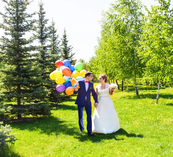 Beautiful bride and groom on a park with colorful balloons — Stock Photo, Image