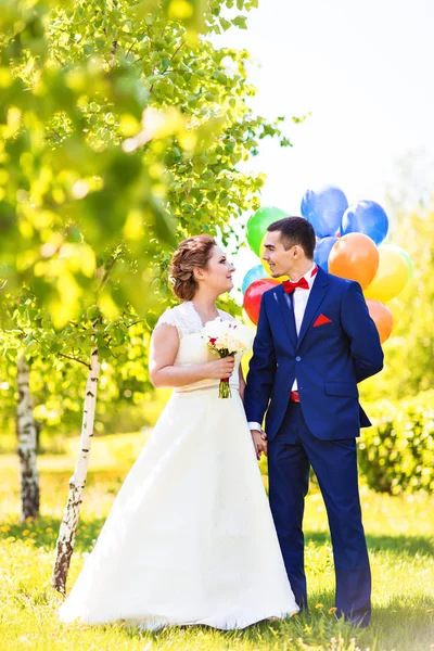 Beautiful bride and groom on a park with colorful balloons — Stock Photo, Image