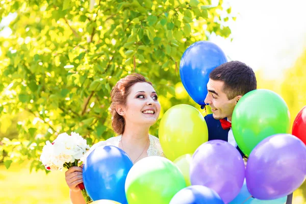 Schöne Braut und Bräutigam auf einem Park mit bunten Luftballons — Stockfoto