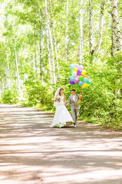 Pięknej narzeczonej trzymając kilka balonów w parku. Pary młodej i pana młodego z balonów. Nowożeńcy z balonów na zewnątrz — Zdjęcie stockowe