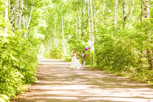 Beautiful bride holding bunch of balloons in the park. Couple of bride and groom with balloons. Newlyweds with balloons outdoors