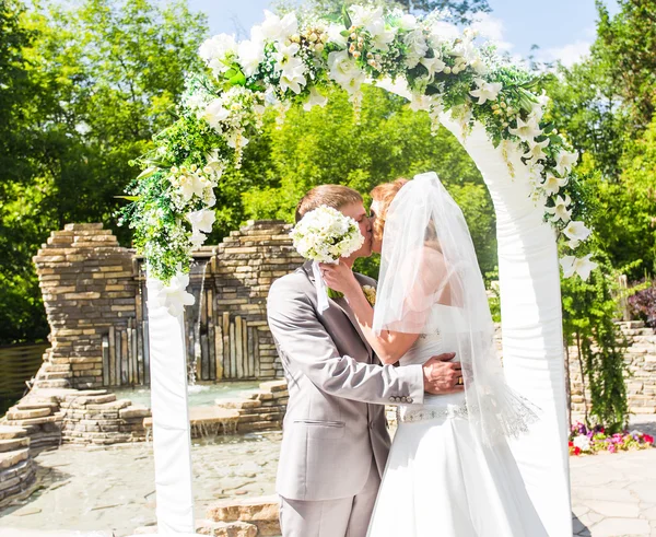 Eerste kus van nieuw echtpaar onder huwelijksboog — Stockfoto