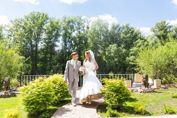 Noiva e noivo no dia do casamento andando ao ar livre na natureza de primavera. Casal nupcial, mulher recém-casada feliz e homem abraçando no parque verde. Casal de amor ao ar livre — Fotografia de Stock