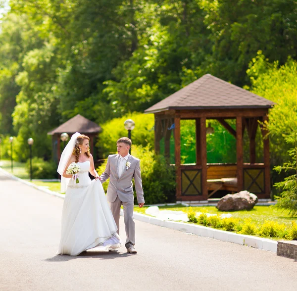 Novia y novio en el día de la boda caminando al aire libre en la naturaleza de primavera. Pareja nupcial, feliz mujer recién casada y hombre abrazándose en el parque verde. Amar pareja de boda al aire libre —  Fotos de Stock