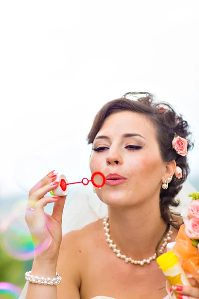 Beautiful bride blowing soap bubbles outdoors — Stock Photo, Image