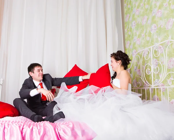 Novia y novio peleando con almohadas en la cama — Foto de Stock