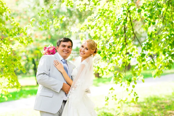 Свадебная пара обнимается, невеста держит букет цветов в руке, жених обнимает ее — стоковое фото