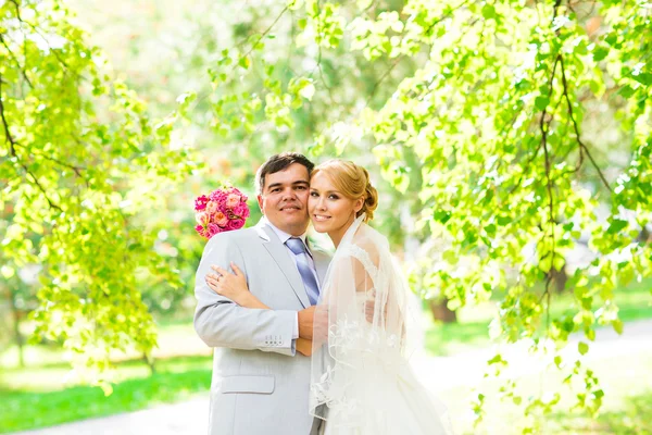 Pareja de boda abrazándose, la novia sosteniendo un ramo de flores en su mano, el novio abrazándola — Foto de Stock