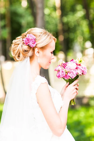 Vackra brud med bröllop bukett blommor utomhus i grön park — Stockfoto