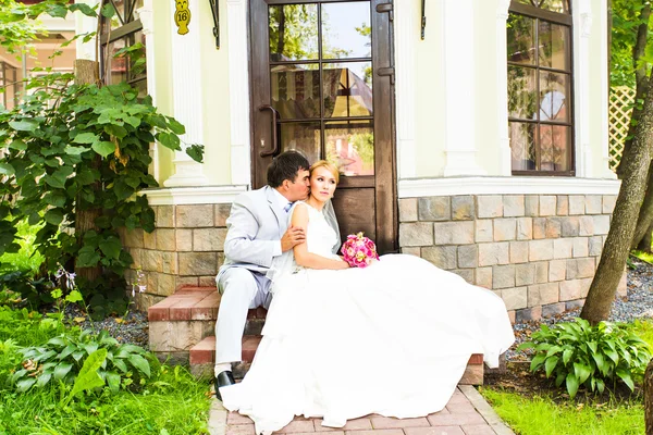 Casal em traje de casamento com um buquê de flores e vegetação está nas mãos, a noiva eo noivo beijando — Fotografia de Stock