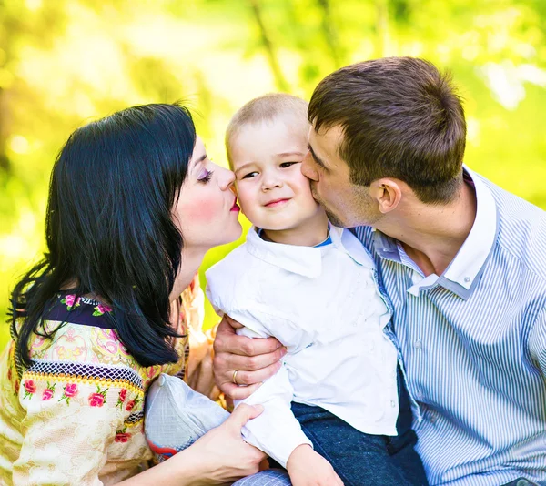 Glückliche Mutter und Vater küssen ihren kleinen Sohn im Park — Stockfoto