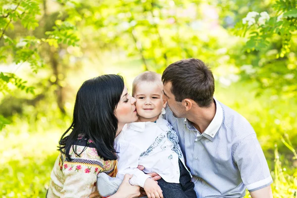 Glückliche Mutter und Vater küssen ihren kleinen Sohn im Park — Stockfoto