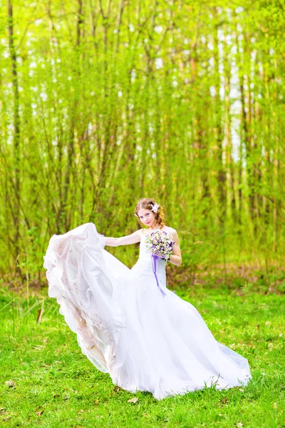 Весільна сукня нареченої розвивається в повітрі проти зеленого поля — стокове фото