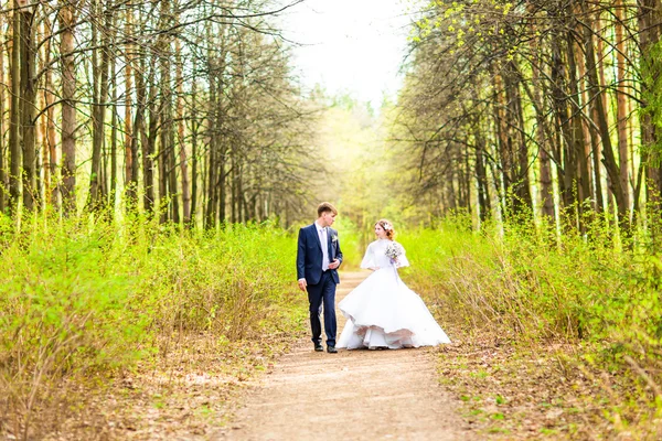 Noiva e noivo no dia do casamento andando ao ar livre na natureza de primavera. Casal nupcial, mulher recém-casada feliz e homem abraçando no parque verde. Casal de amor ao ar livre . — Fotografia de Stock