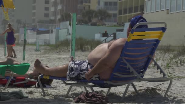 Zwaarlijvige man loungen op een strand — Stockvideo