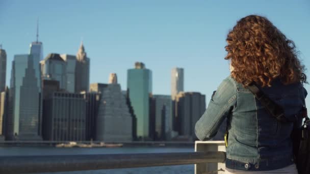 Una hermosa mujer cerca del puente de Brooklyn mira hacia Manhattan — Vídeos de Stock