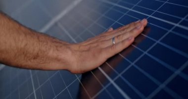 Erkek mühendisin ellerinin fotovoltaik elektrikli güneş paneli bataryasına dokunuşunun yakın görüntüsü. Güneş parkı kavramı, yeşil yenilenebilir enerji ve yenilikler.