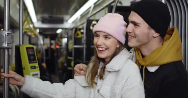 Un tipo feliz abrazando a una chica atractiva mientras van en transporte público. Millennial alegre pareja hablando y sonriendo mientras mira a la ventana en la noche. Concepto de relación. — Vídeo de stock