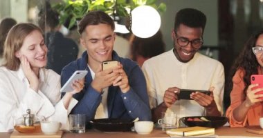 Akıllı telefonlarını kullanan ve birlikte vakit geçirirken gülümseyen genç güzel insanlar. Kafede otururken sosyal ağlarda sohbet eden bin yıllık neşeli arkadaşların mahsül görüşü.