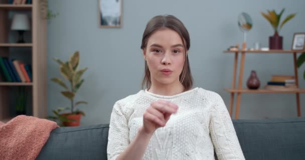 Crop view of woman showing with deaf-mute sign language no racism while looking to camera. Femme soutenant l'égalité et le mouvement des droits de l'homme alors qu'elle était assise sur le canapé à la maison. — Video