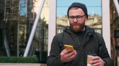 Sakallı adam sesli mesaj bırakıyor ya da sanal asistan uygulaması kullanıyor ve ekrana bakarken gülüyor. Gözlüklü yakışıklı adam sokakta yürürken konuşuyor ve akıllı telefon kullanıyor..