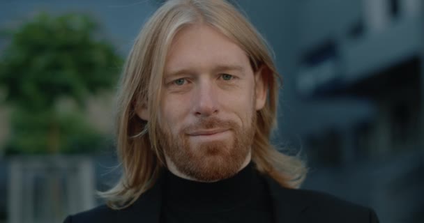 Retrato de un buen hombre de negocios barbudo mirando a la cámara. Vista de cerca del exitoso hombre de pelo largo en traje posando mientras está de pie en la calle. Concepto de personas en la cabeza. — Vídeos de Stock