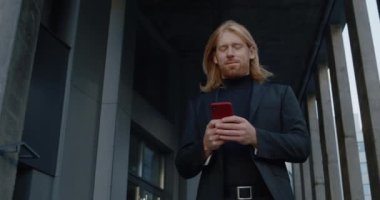 Akıllı telefon kullanıp gülümseyen güzel sakallı bir adamın portresi. İş adamının dışarıda dikilirken yazı yazıp ekrana dokunuşunun alt görüntüsü. Başarılı insanlar kavramı.