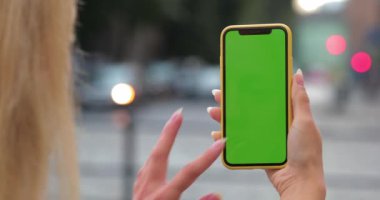 Şablon ekran ile akıllı telefon tutan sarışın kadın görüntüsü. Caddede yeşil ekran telefon kullanan bir kadının üstten görünüşü. Arkaplanda giden arabalar.